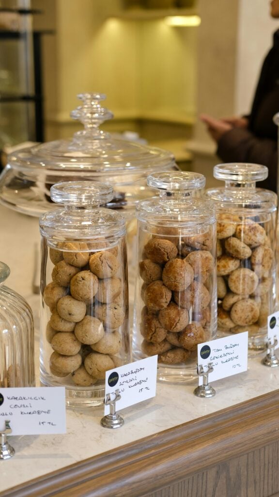 Tall cylinder glass jars on a counter filled with cookies and labeled for a bridal shower tea party idea.