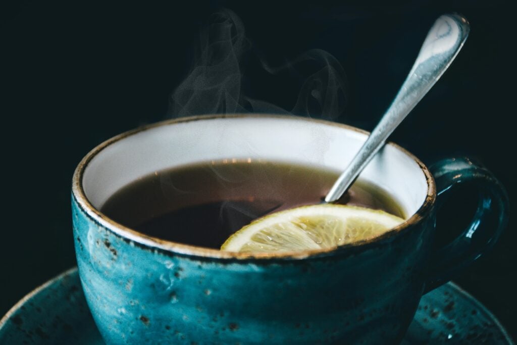 A turquoise teacup with the best black tea, a lemon slice, and a silver spoon.