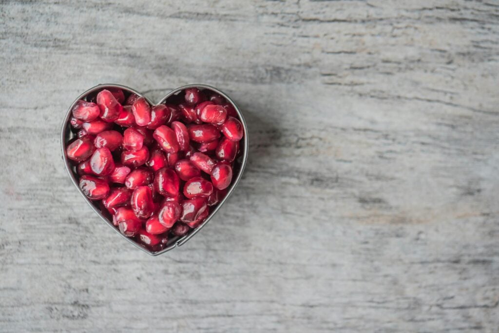 Fresh pomegranate seeds in a heart-shaped tin on a marble table.