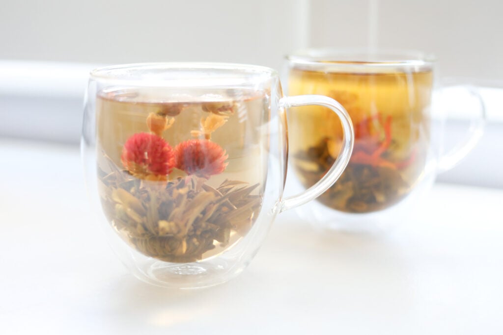Two double-walled glass mugs with blooming green tea flowers that have green tea health benefits.