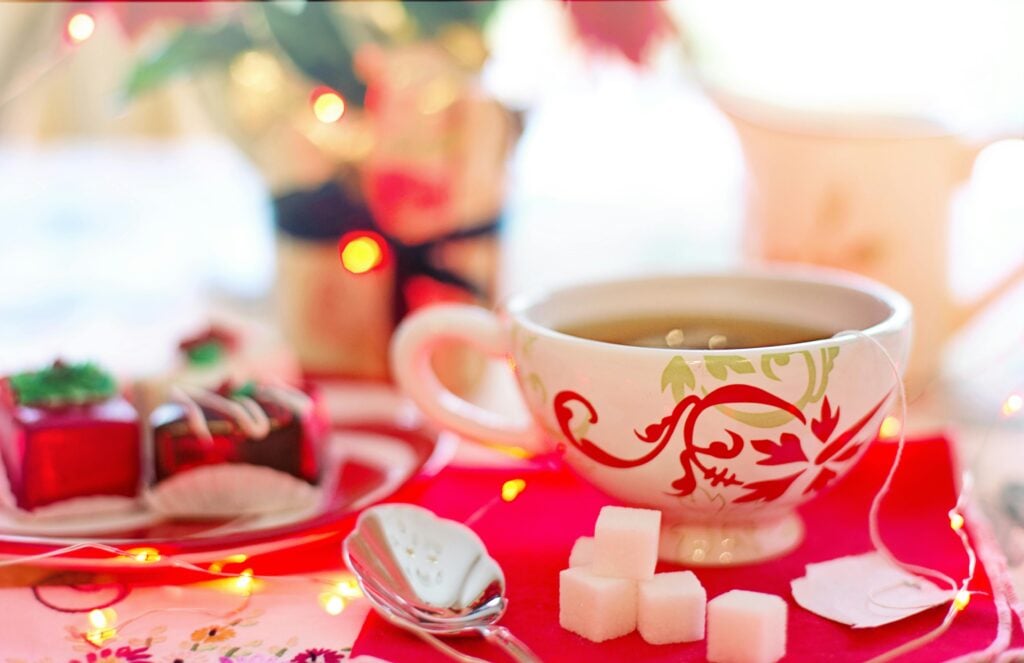 Holiday tea party cup with sugar cubes and red and green decor with fairy lights and holiday petit fours.
