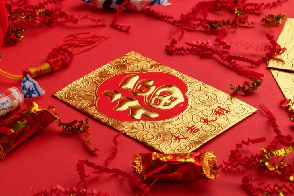 Gold and red New Year Chinese money envelope on a red table with red confetti and red and gold wrapped candies.