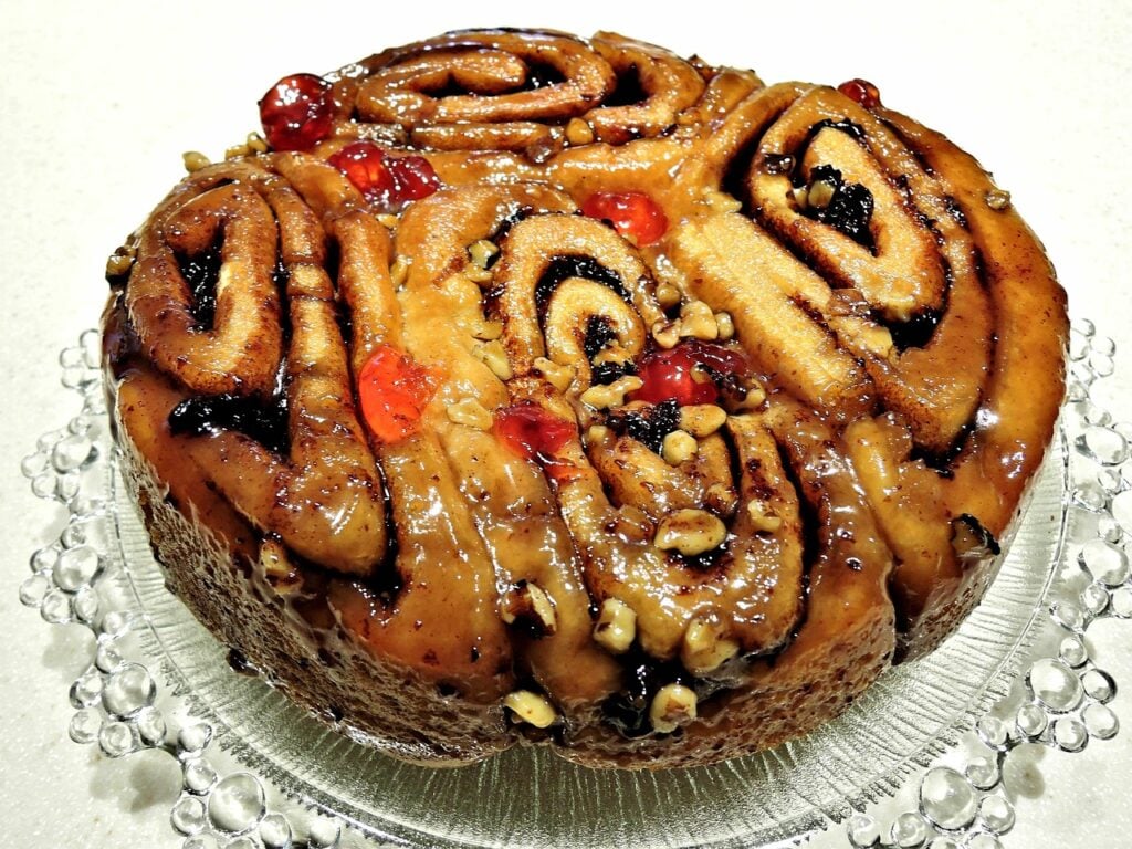 Chelsea buns on a glass plate with candied cherries, raisins, dried fruit, and nuts. 