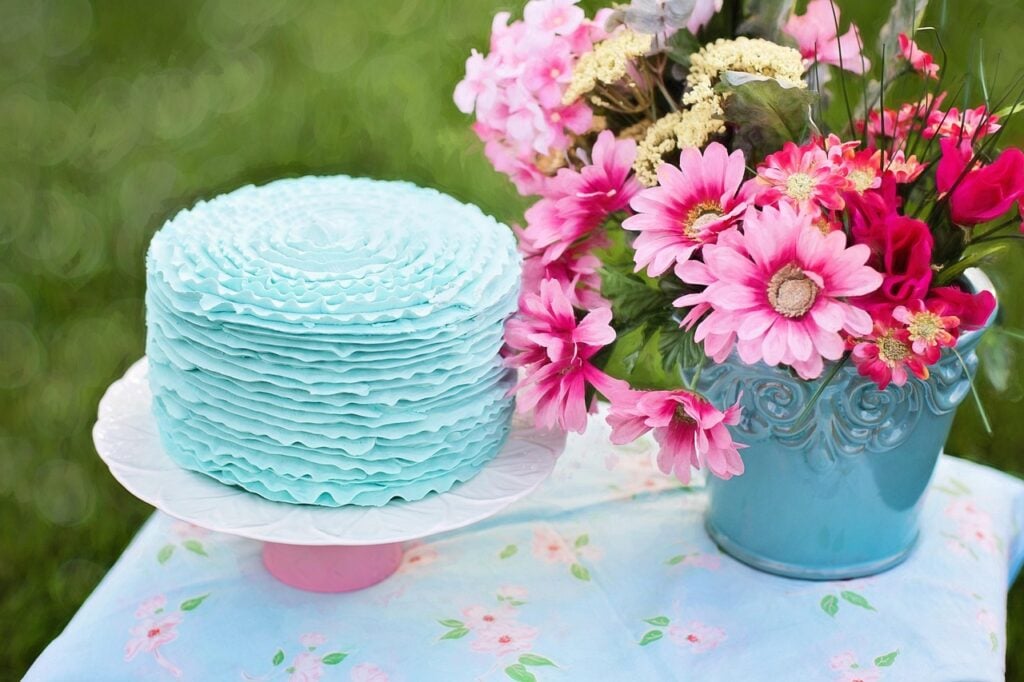 A garden tea party table with a blue cake, fresh flowers, and a blue floral tablecloth.