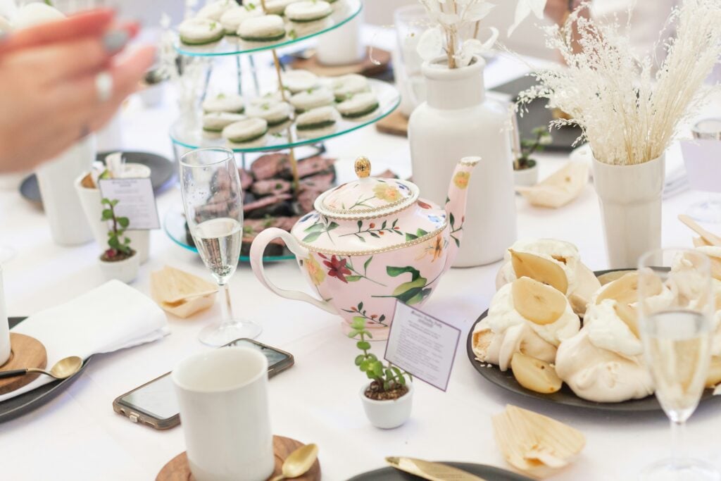 A garden tea party outdoor display with white linens, a tiered tea stand, place settings, and a teapot.