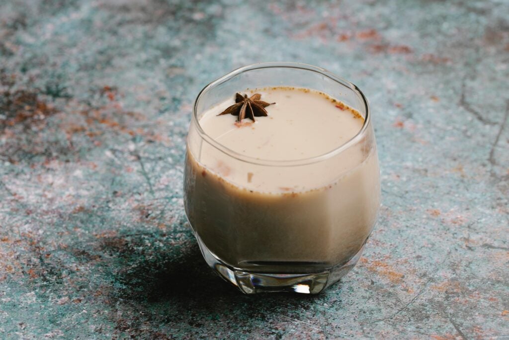 A glass cup of masala chai with a star anise floating on the surface.
