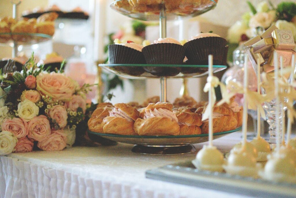 A luxurious display of pastries and sweets on a table with fresh flowers for a charity garden tea party.