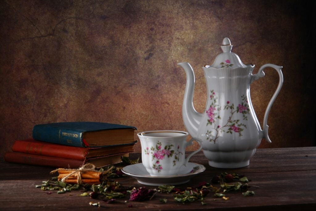 A tall white porcelain teapot and teacup on a wooden table with a small stack of books for a garden tea party idea.