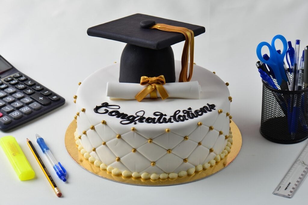 A white and gold graduation cake with a black hat and white diploma as an idea for a garden tea party dessert.