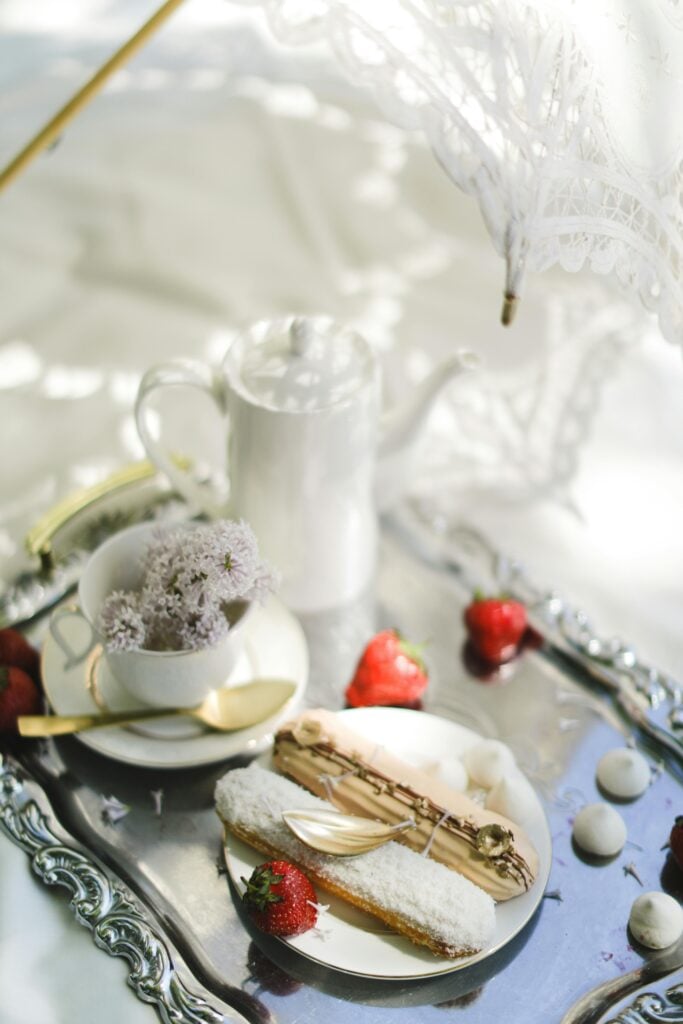 A white lace parasol shading a silver tray with garden tea party pastries and tea.