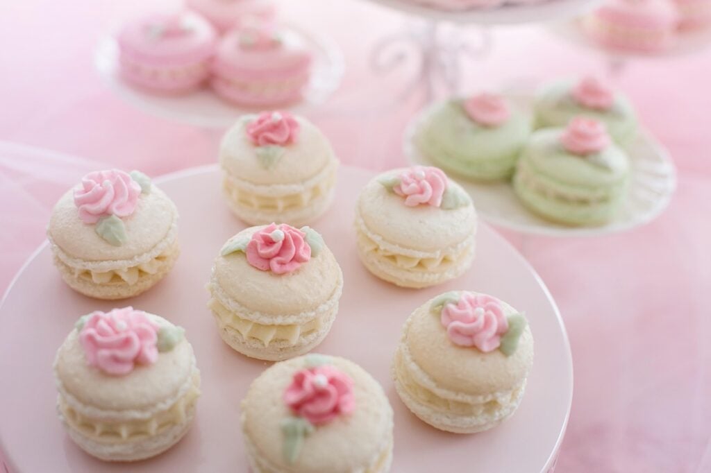 White macarons with pink piped flowers on a white pedestal stand for a Mother’s Day garden tea party.