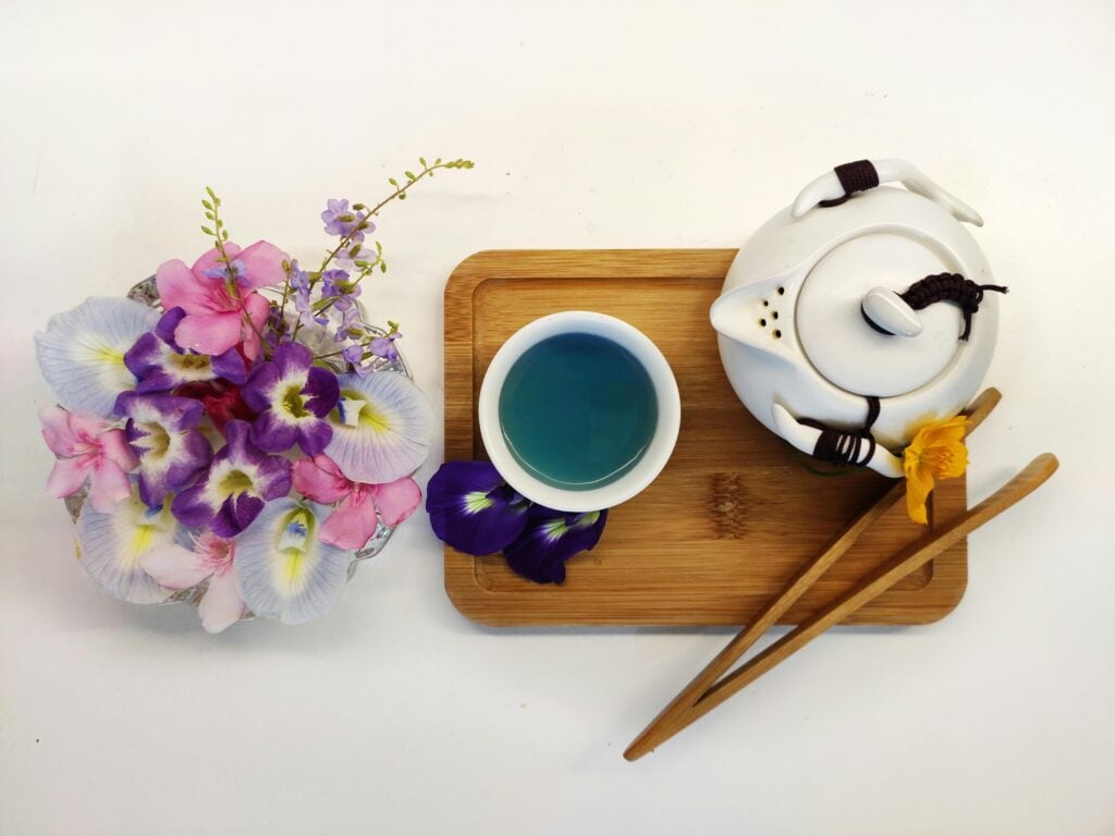 A top-down view of a white teacup with blue butterfly pea tea, a teapot, and a bouquet of flowers featured as a unique tea from around the world.