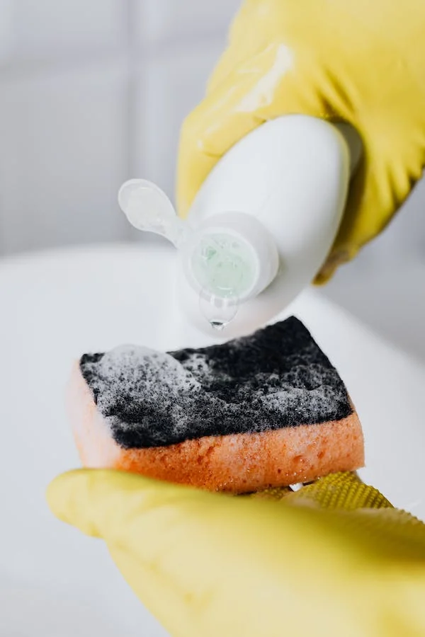 Hands with yellow dish gloves holding sponge and bottle of dish soap