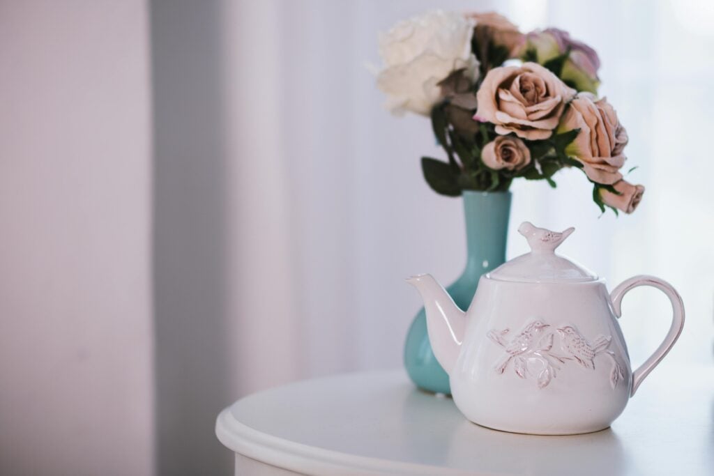 White ceramic teapot with birds on table with flowers