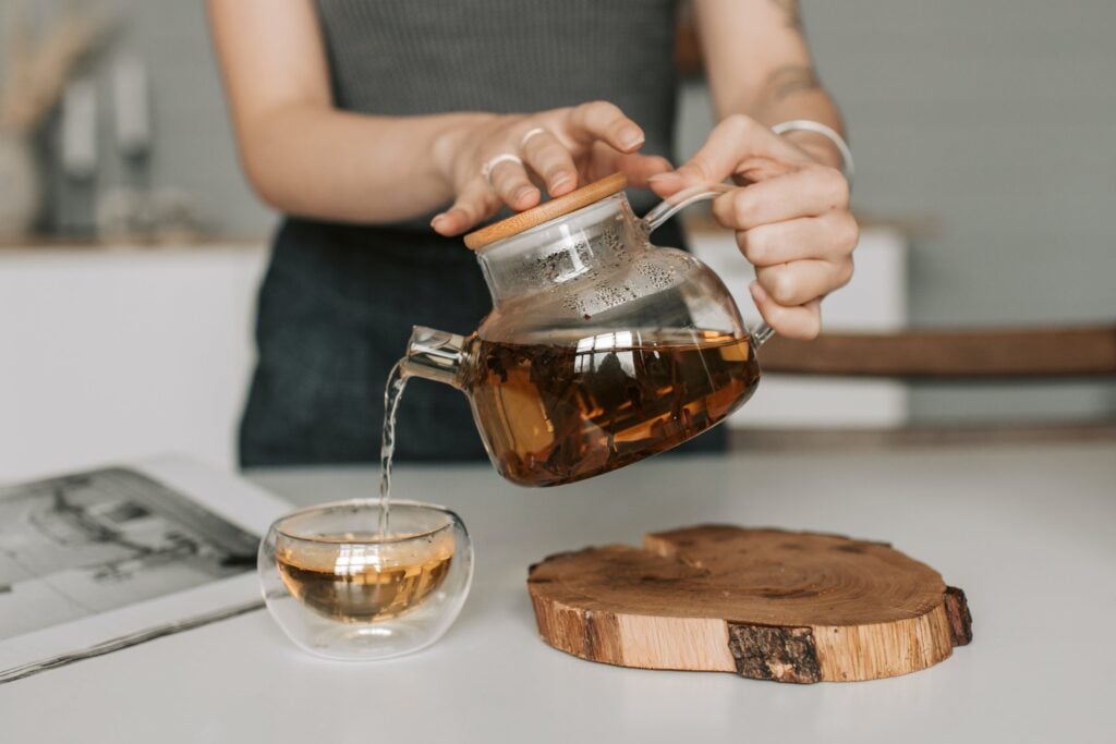 A person learning how to steep green tea while pouring green tea into a teacup