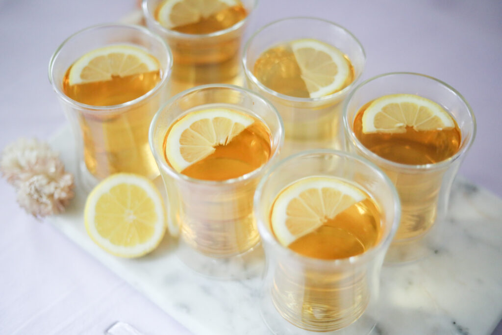 Six borosilicate glass teacups with steeped green tea and lemon slices