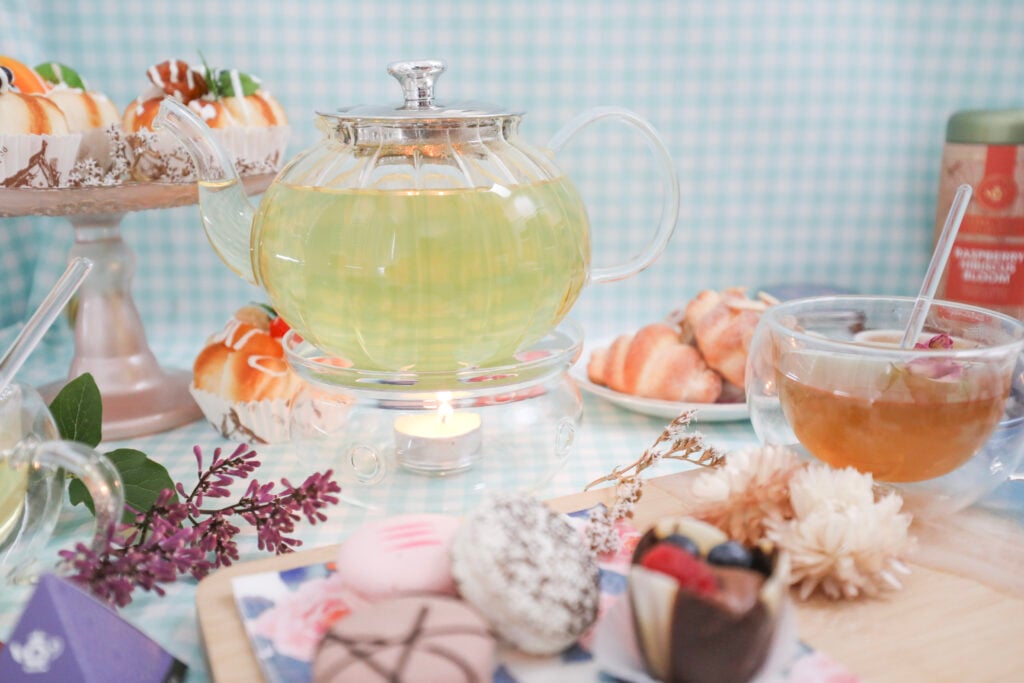 Borosilicate glass teapot with green tea surrounded by sweet treats and flowers