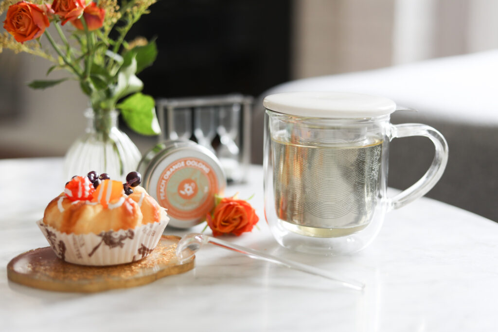 Tea on the go mug with infuser on a white countertop next to dessert and flowers