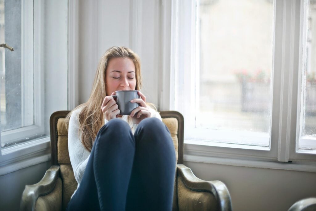 A woman smiling, curled up in a chair holding a cup of tea.