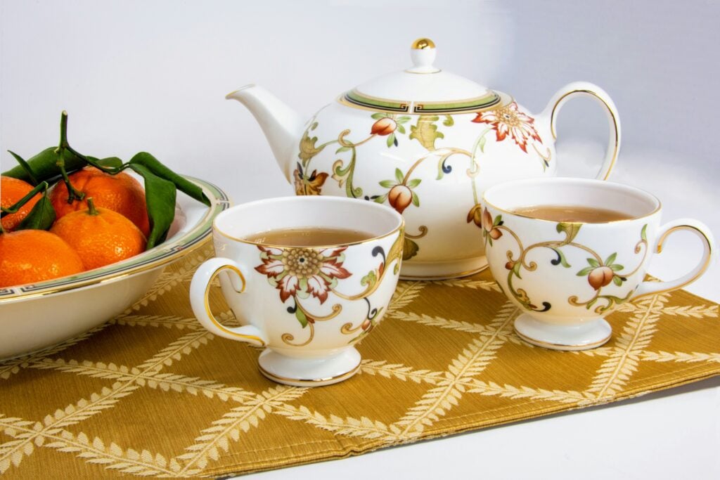 Porcelain teaware with a bowl of mandarin oranges displayed on a gold table runner.