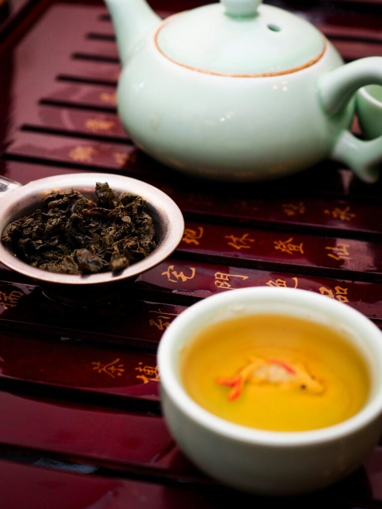 A teapot, teacup and used tea leaves on a bamboo tray