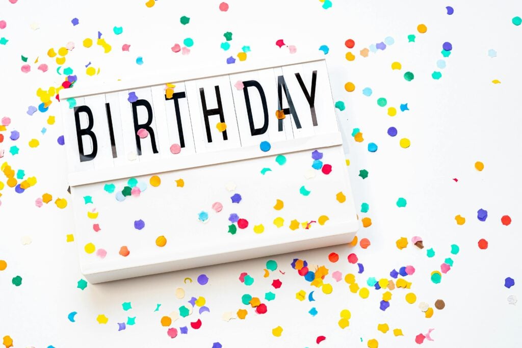 A white birthday sign surrounded by colorful confetti as inspiration for tea parties for birthdays.