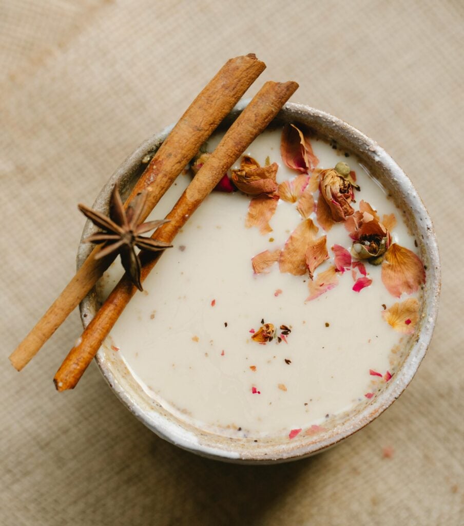 Kashmiri Noon Chai unique tea with a pink hue, sprinkled with rose petals and garnished with star anise and cinnamon sticks. 