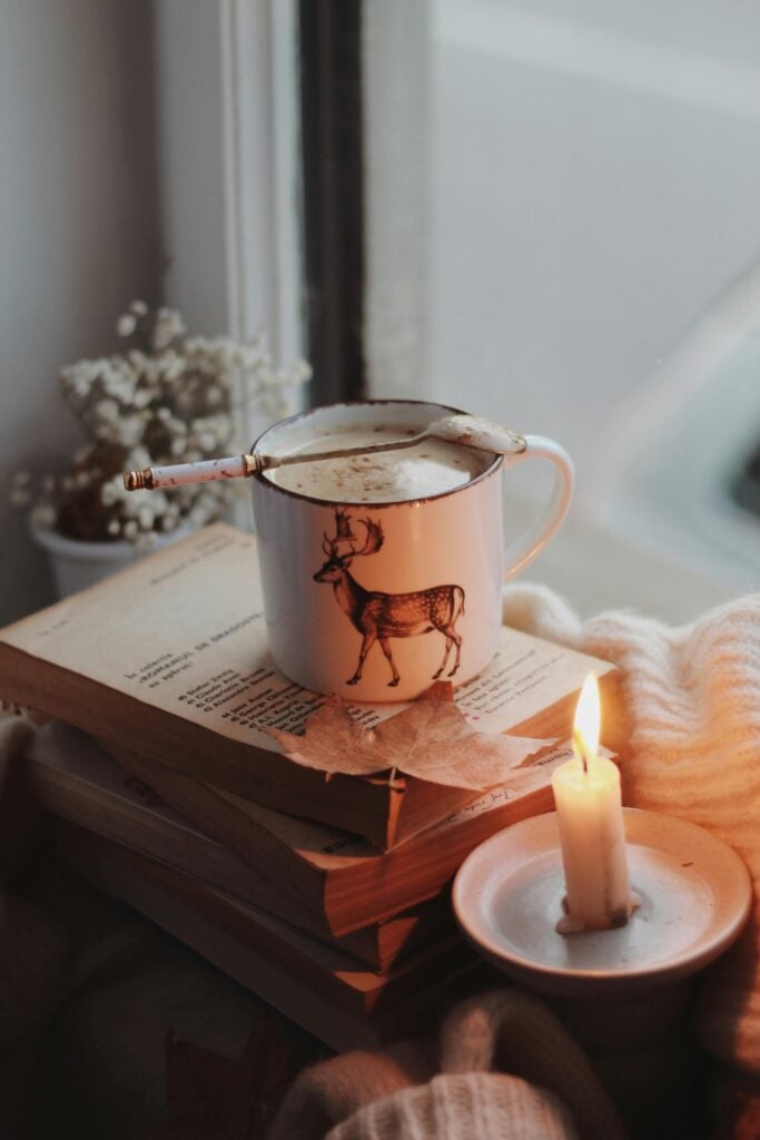 Chai tea cocktail recipe in a white mug with a reindeer on a stack of books next to a lit candle.