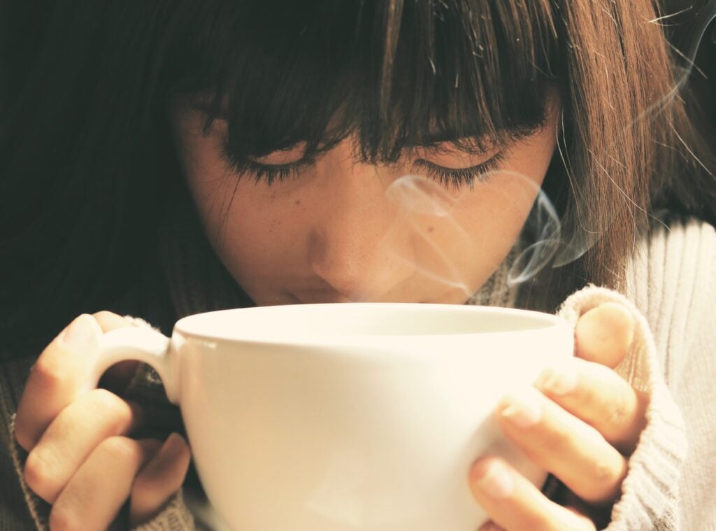 A closeup of a woman drinking a steaming cup of tea.