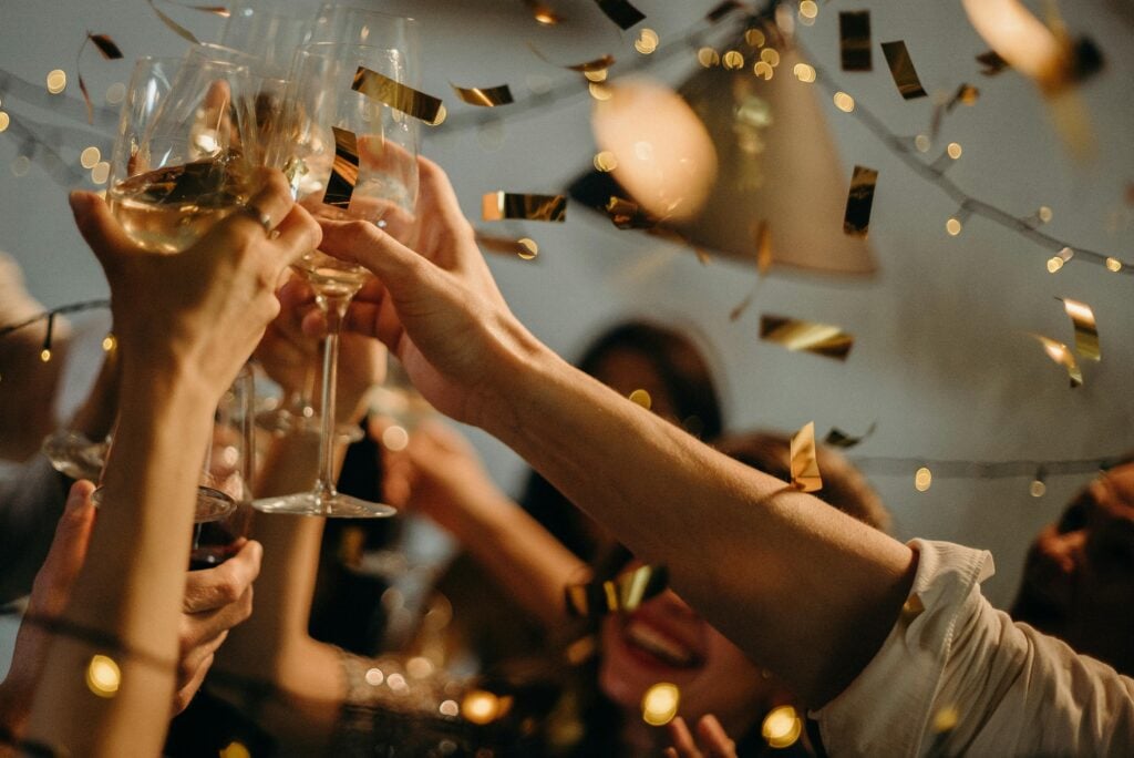 People toasting champagne glasses with gold confetti as a holiday tea party idea.