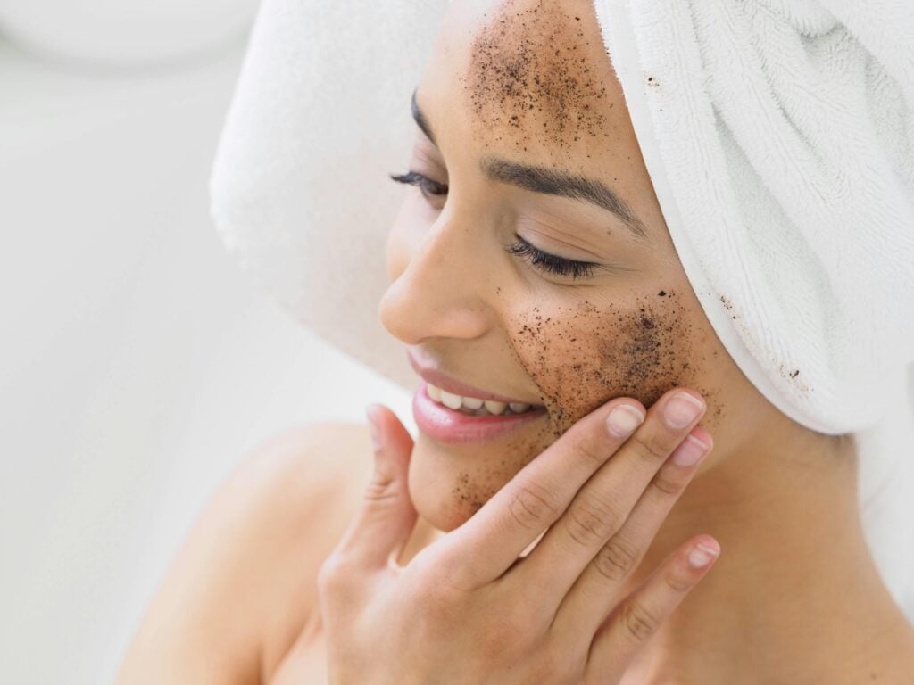A woman with a white hair towel exfoliating her face with tea for skin and sugar.