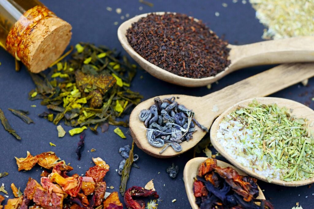 Dried herbs, fruits, and spices scattered on a blue table with wooden spoons.