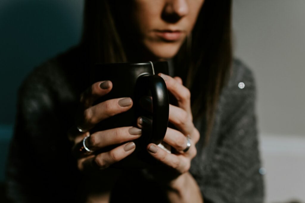 A woman with dark hair in a dark grey sweater holding a black cup of tea with a tea bag that may have microplastics.