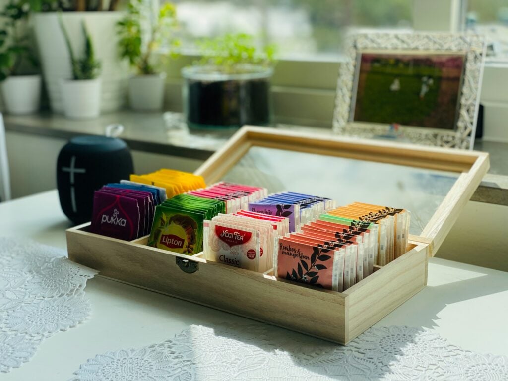 A wooden tea case on a white table stocked with tea bags from different popular tea companies.