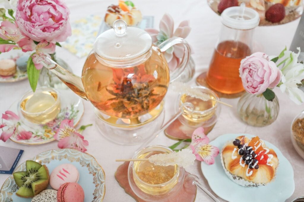 The Celebration glass tea set with four double-walled handle-free cups on a table with pasties and flowers.