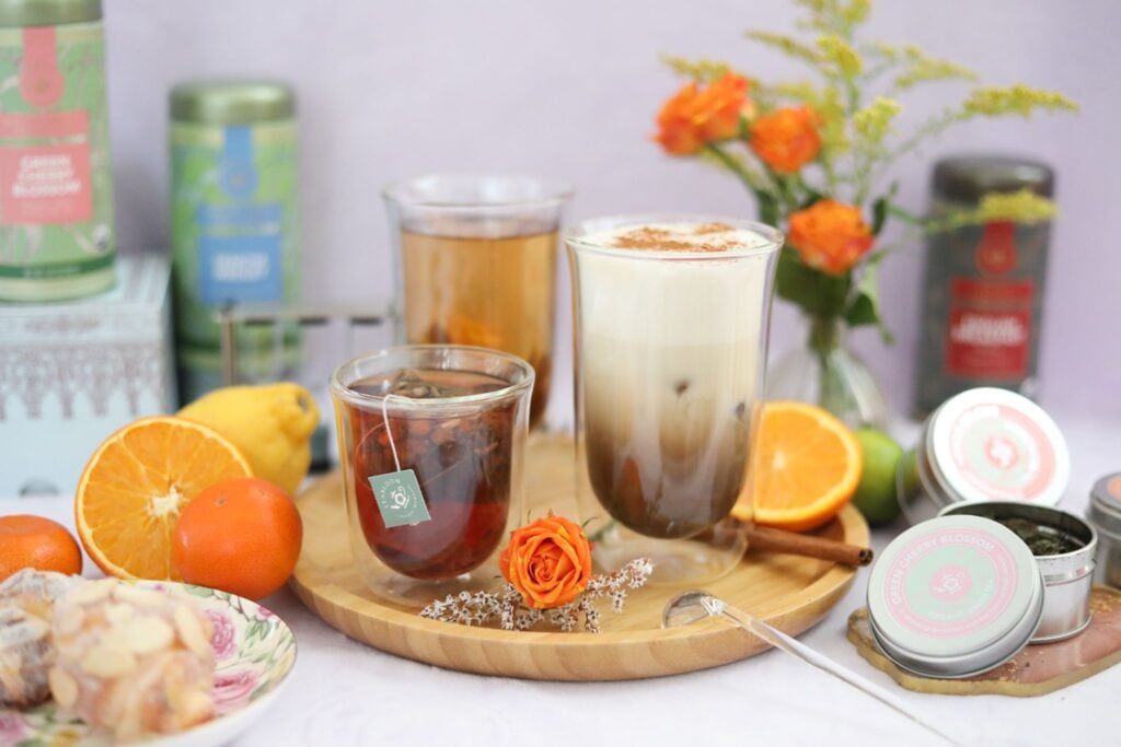 Tulip-shaped glasses in three sizes with different beverages on a table with tea, oranges, and pastries.