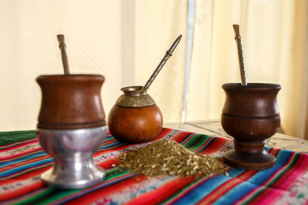Three maté gourds on a colorful tapestry with a small pile of maté leaves as an example of one of the best teas for energy.