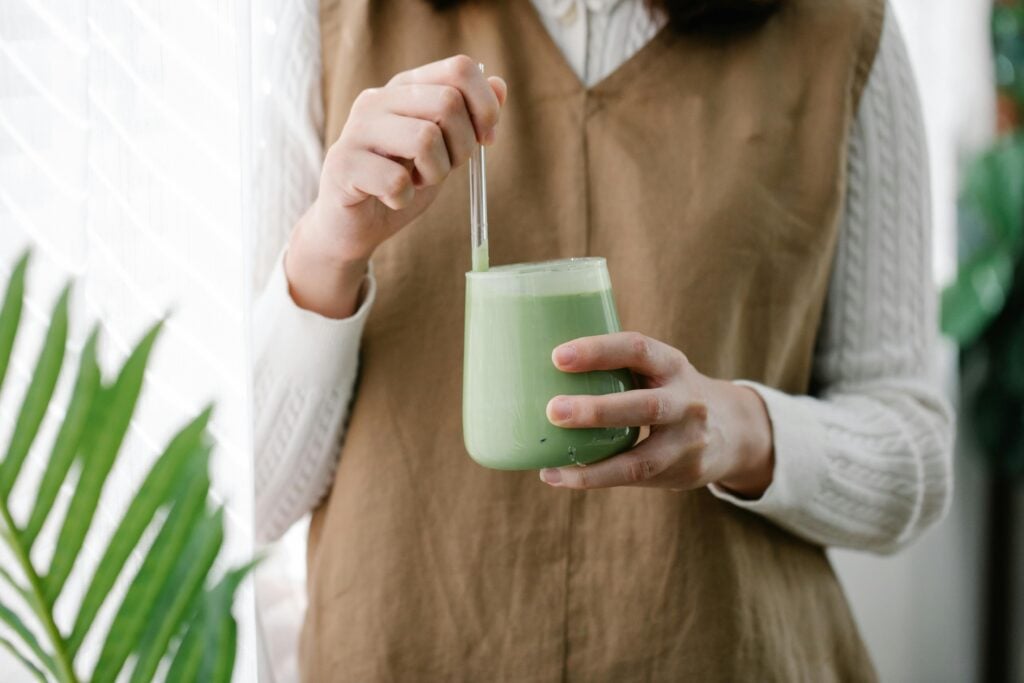 A close-up of a woman in a white shirt and brown dress with a glass cup of matcha, as one of the best teas for energy.