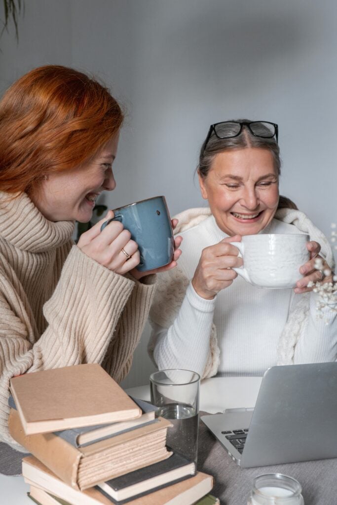 A mother and daughter holding tea cups and laughing while sharing tea jokes.